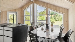 Eine moderne Küche mit einer zentralen Kochinsel, großen Fenstern und einem Essbereich mit Stühlen und Tisch.