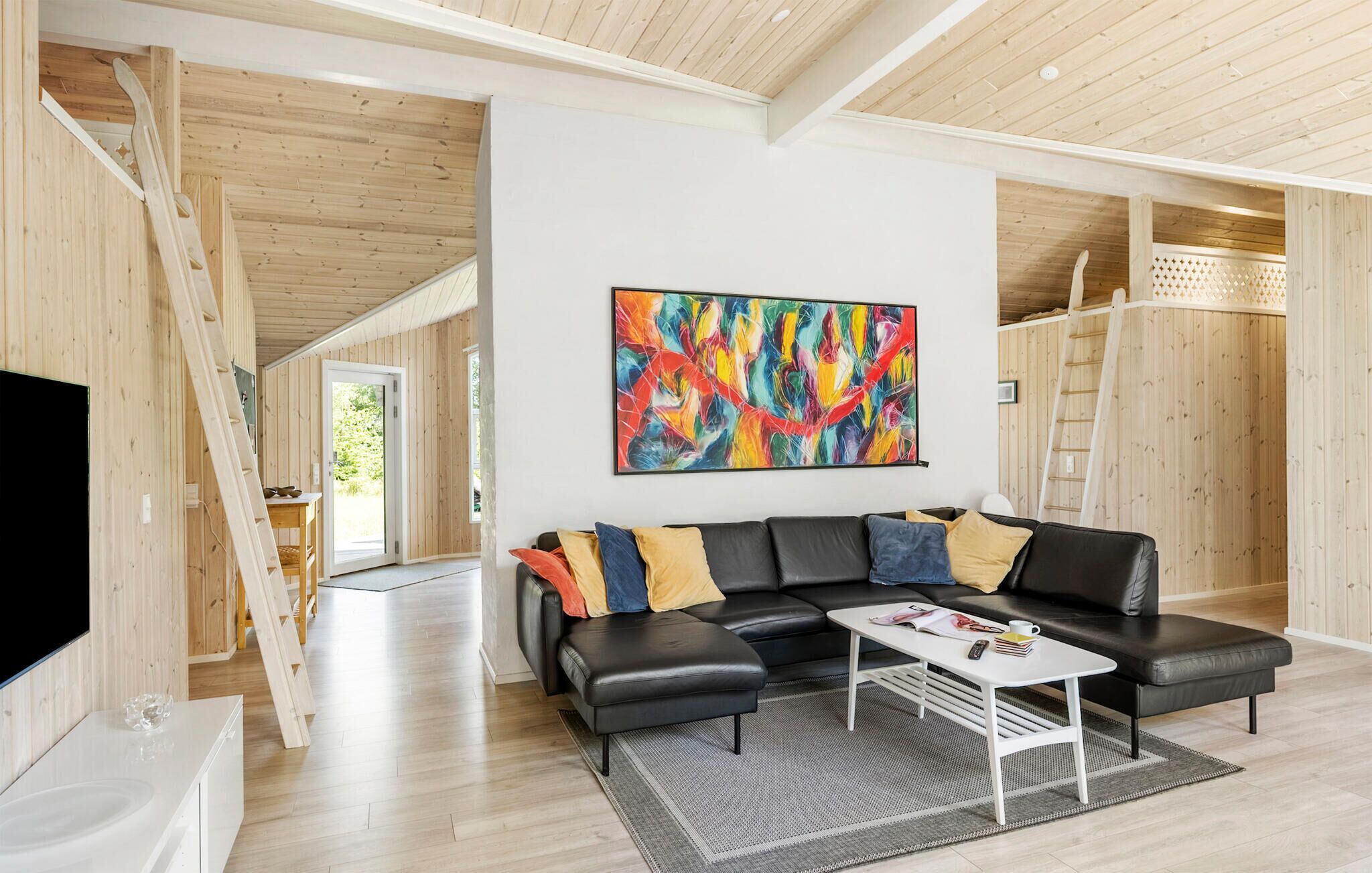 Un salon moderne avec un canapé en cuir noir, une table basse blanche et un tableau abstrait aux couleurs vives.