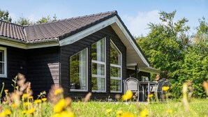 Ein Holzhäuschen mit großen Fenstern und einer Veranda mit Sitzgelegenheiten.