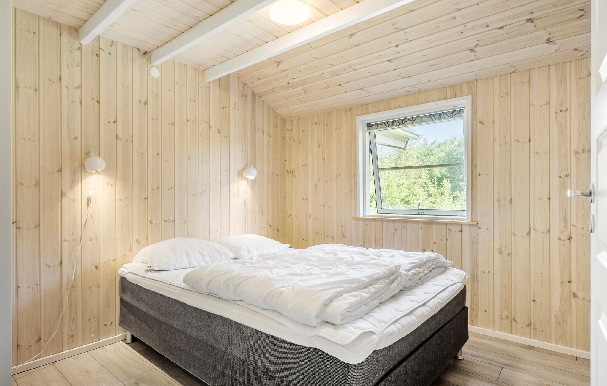 A bedroom with a bed, wooden walls, a window, and a ceiling light.