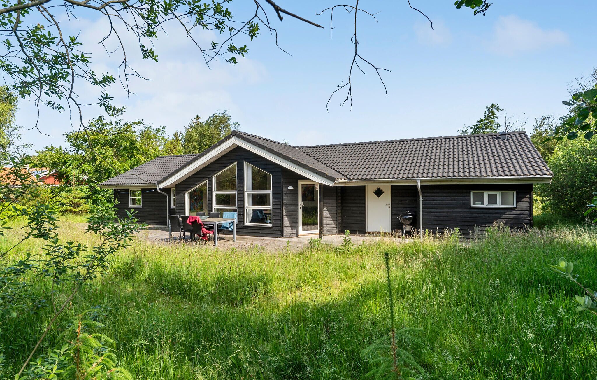 A cabin with a large deck, a covered outdoor seating area, and a barbecue grill.