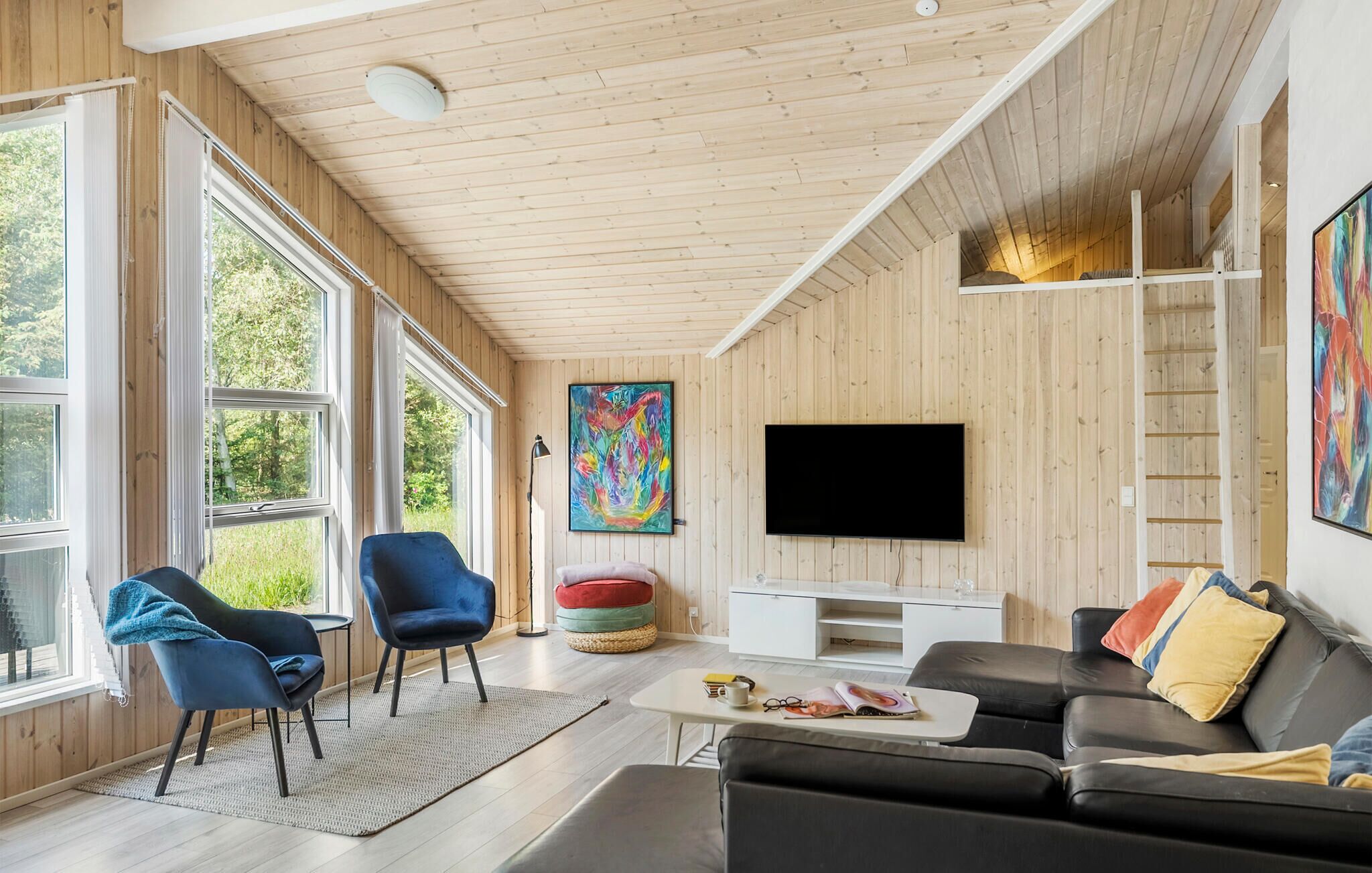 A modern living room with large windows, a flat-screen TV, and a cozy seating area.