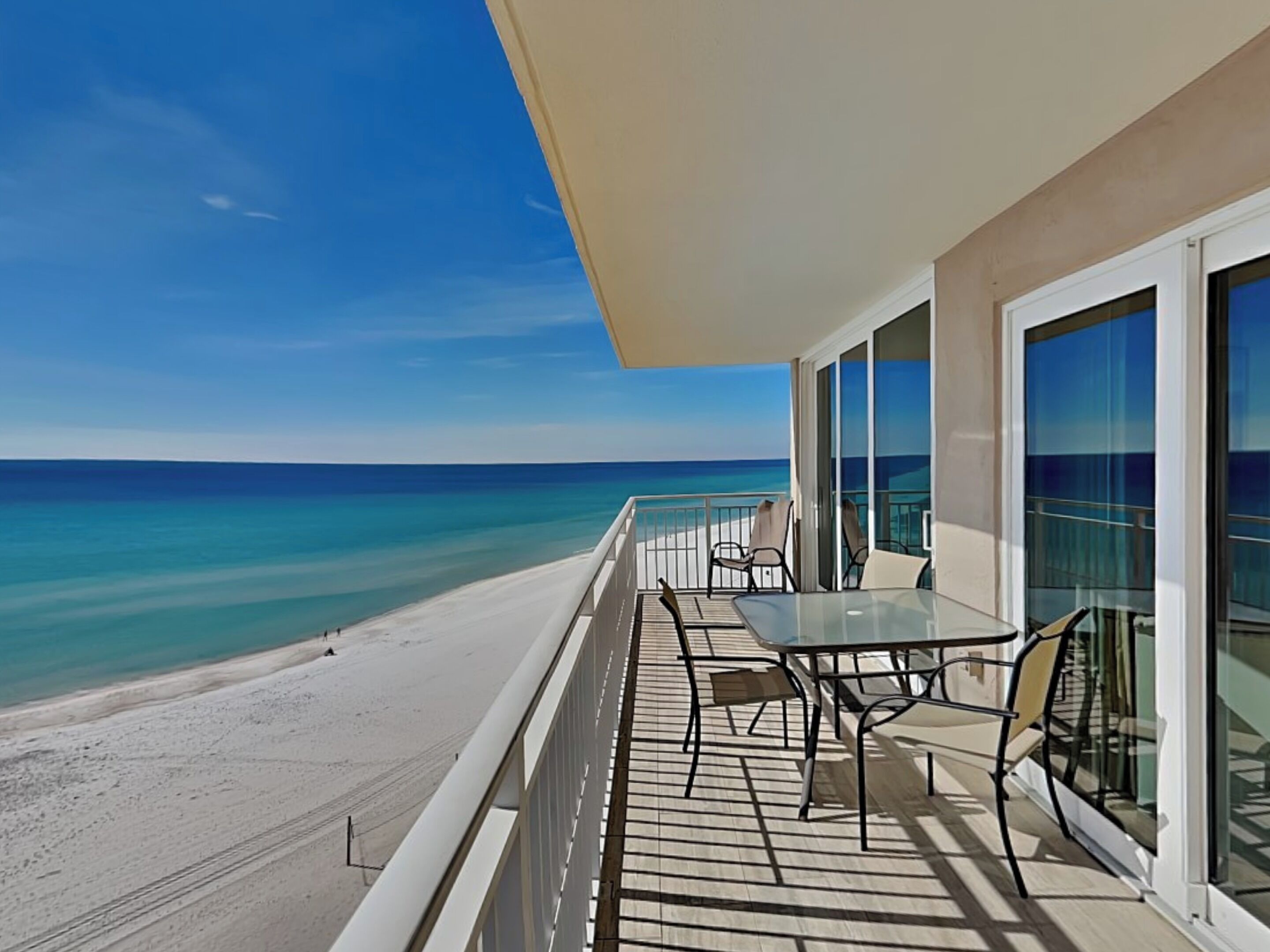 Ein Balkon mit Glastisch und Stühlen mit Blick auf Strand und Meer.