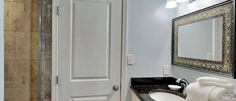 Un baño con una puerta blanca, un lavabo con encimera negra y un espejo con marco decorativo.