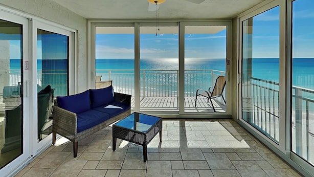 A balcony with a view of the ocean, a ceiling fan, and a glass table. - Dunes of Panama D by Resort Collection (Panama City Beach)