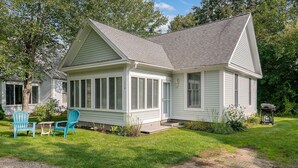 A single-story house with a covered porch, a gravel driveway, and two blue Adirondack chairs. - Cottages at Summer Village, fully furnished cottage, Wi-fi, heated pools, hot tub (Wells)