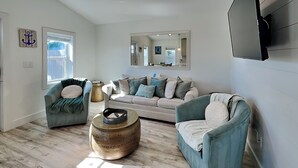 Un salón amplio con un sofá grande, dos sillones, una mesa de centro y un televisor montado en la pared.