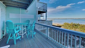 A wooden deck with turquoise chairs and a table, overlooking a calm body of water and a distant shoreline. - Sandcastle Townhomes #24 by Southern Vacation Rentals (Navarre)