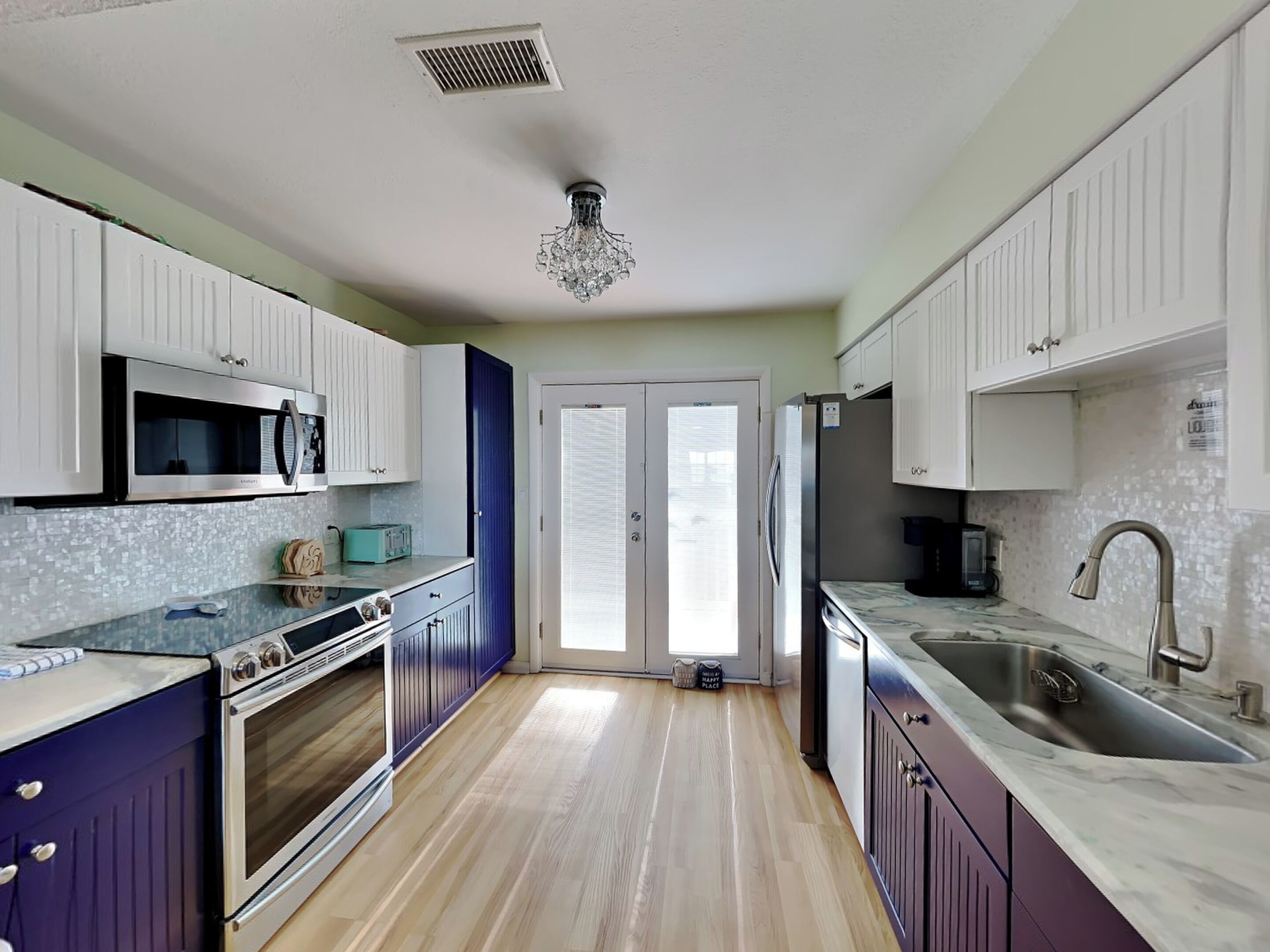 A kitchen with white cabinets, a microwave, a toaster, a sink, and a chandelier.