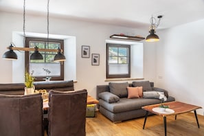 Una sala moderna con sofá, mesa de comedor y sillas, una mesa de centro de madera e iluminación colgante.