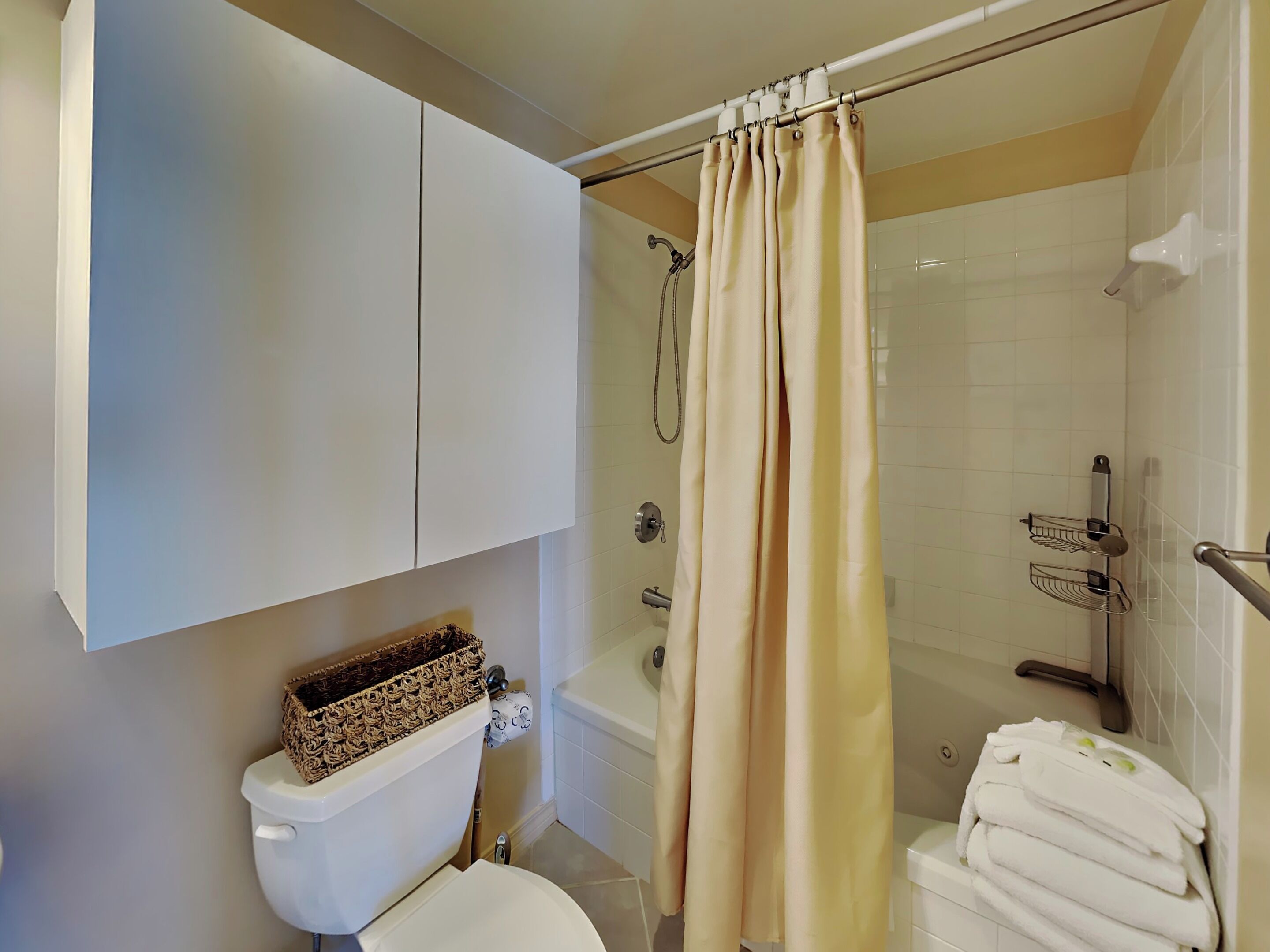A bathroom with a toilet, a shower with a beige curtain, a bathtub, and a towel rack.