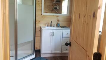 A wooden cabin bathroom with a glass shower door, a sink, cabinets, and a mirror.