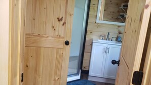 Eine Holztür führt zu einem Badezimmer mit Dusche, Waschbecken und Spiegel.