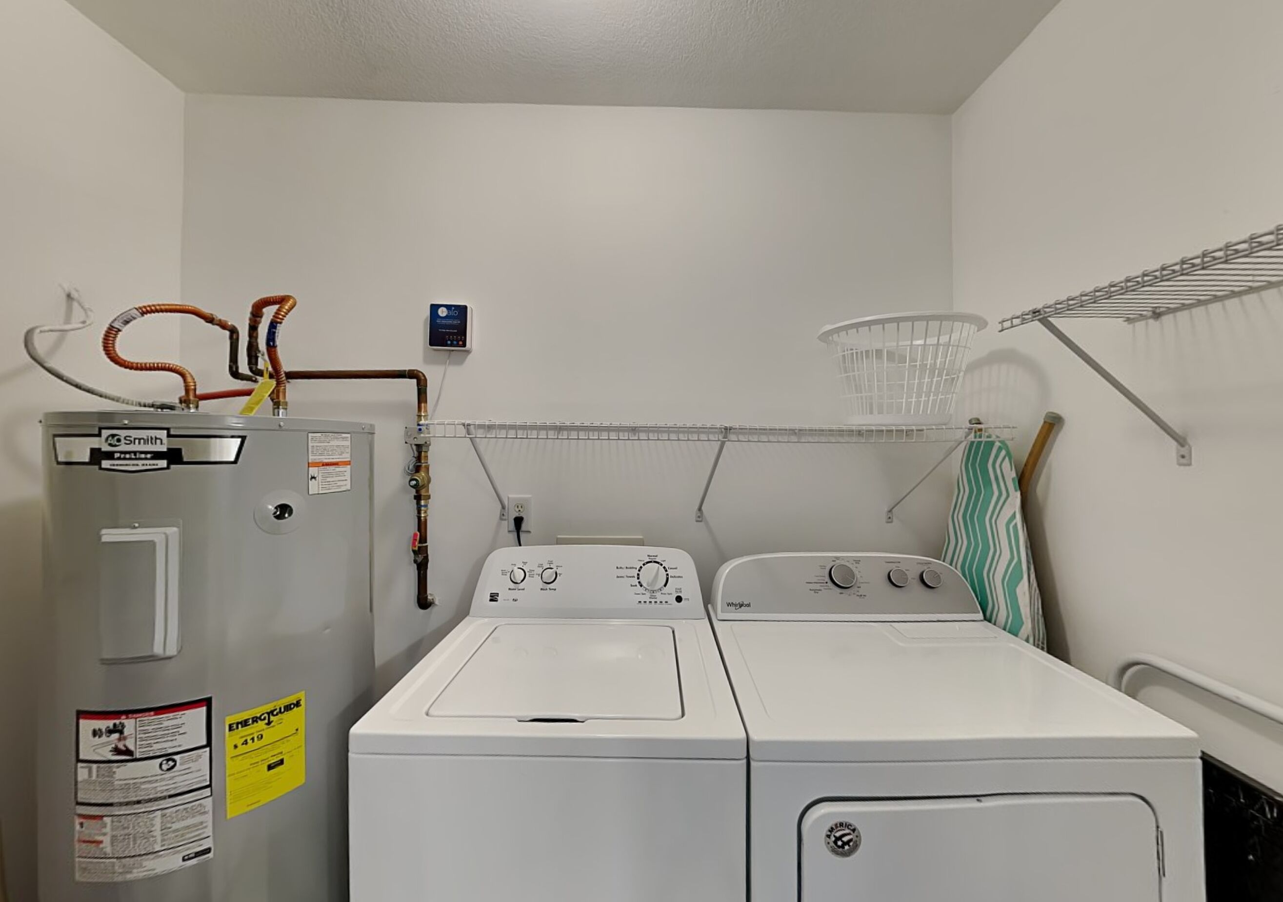 A laundry room with a large industrial washer and dryer, a water heater, and a metal drying rack.