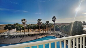 Zona de piscina con sillones de descanso y palmeras, con vista a una playa y el océano.
