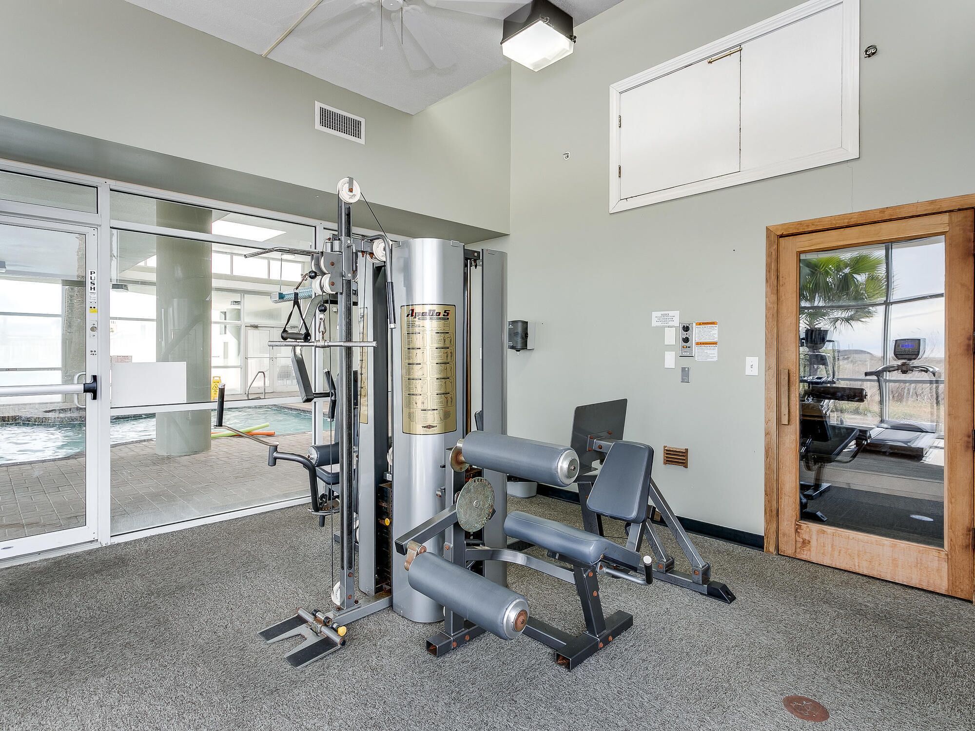 Un gimnasio con equipo de ejercicio, un ventanal y una puerta que da al exterior.