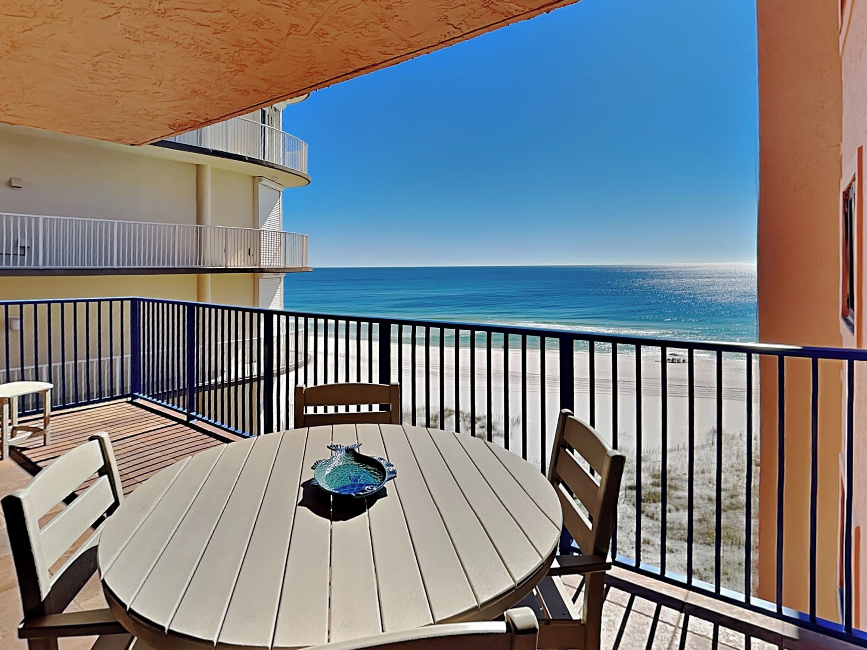 A balcony with a round table and chairs, overlooking a beach.