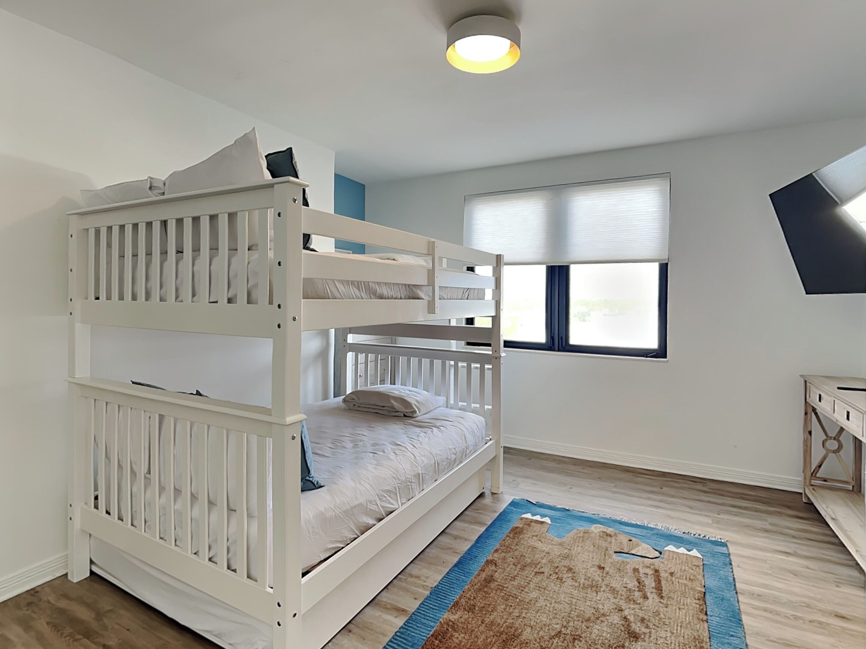 A bunk bed room with a window, a desk, and a rug.