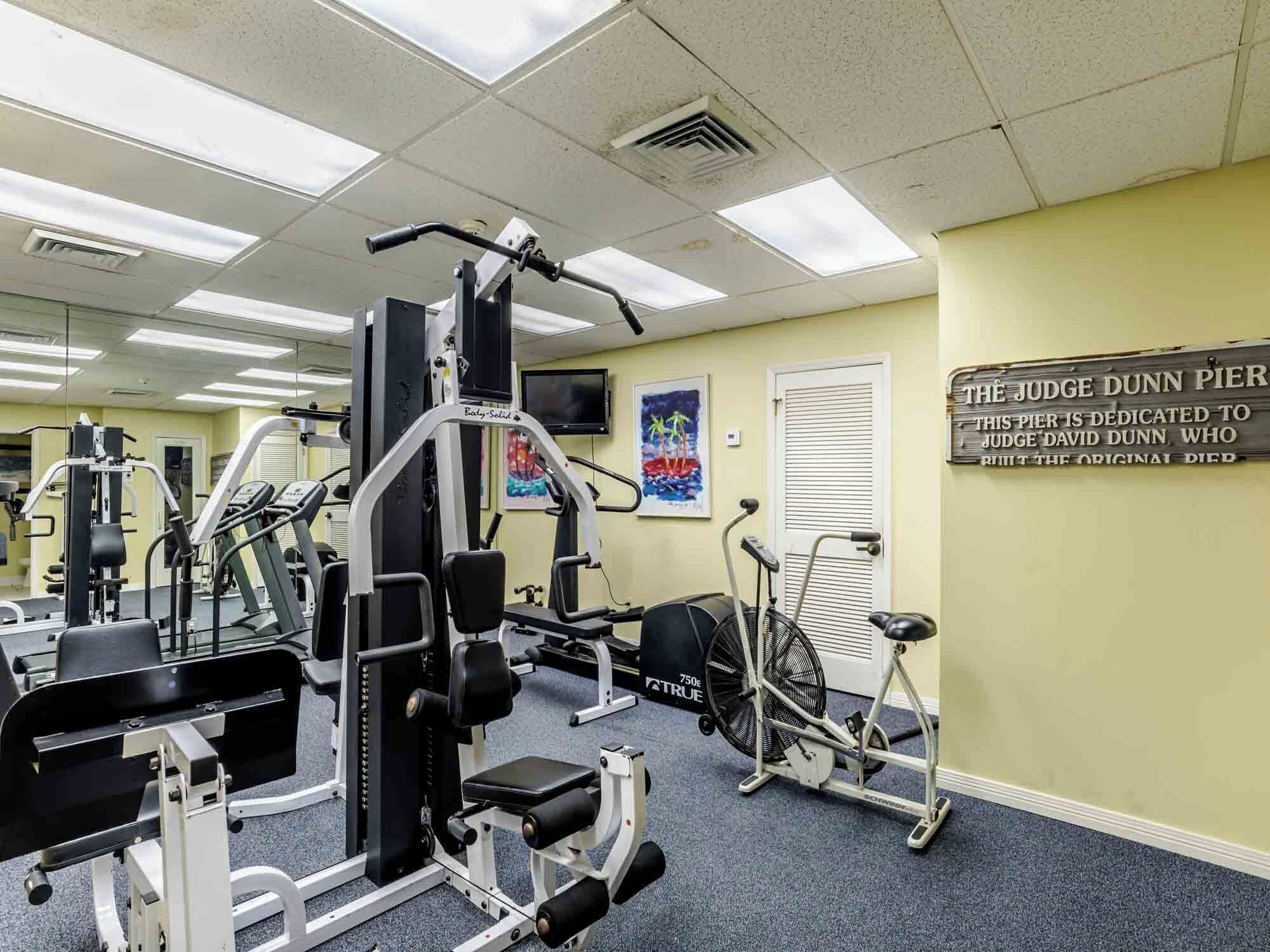 A gym with various exercise equipment, a treadmill, and a sign dedicated to Judge Dunn Pier.