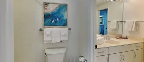 A modern bathroom with a toilet, sink, and shower area. There is a painting above the toilet and a mirror with lights above the sink.