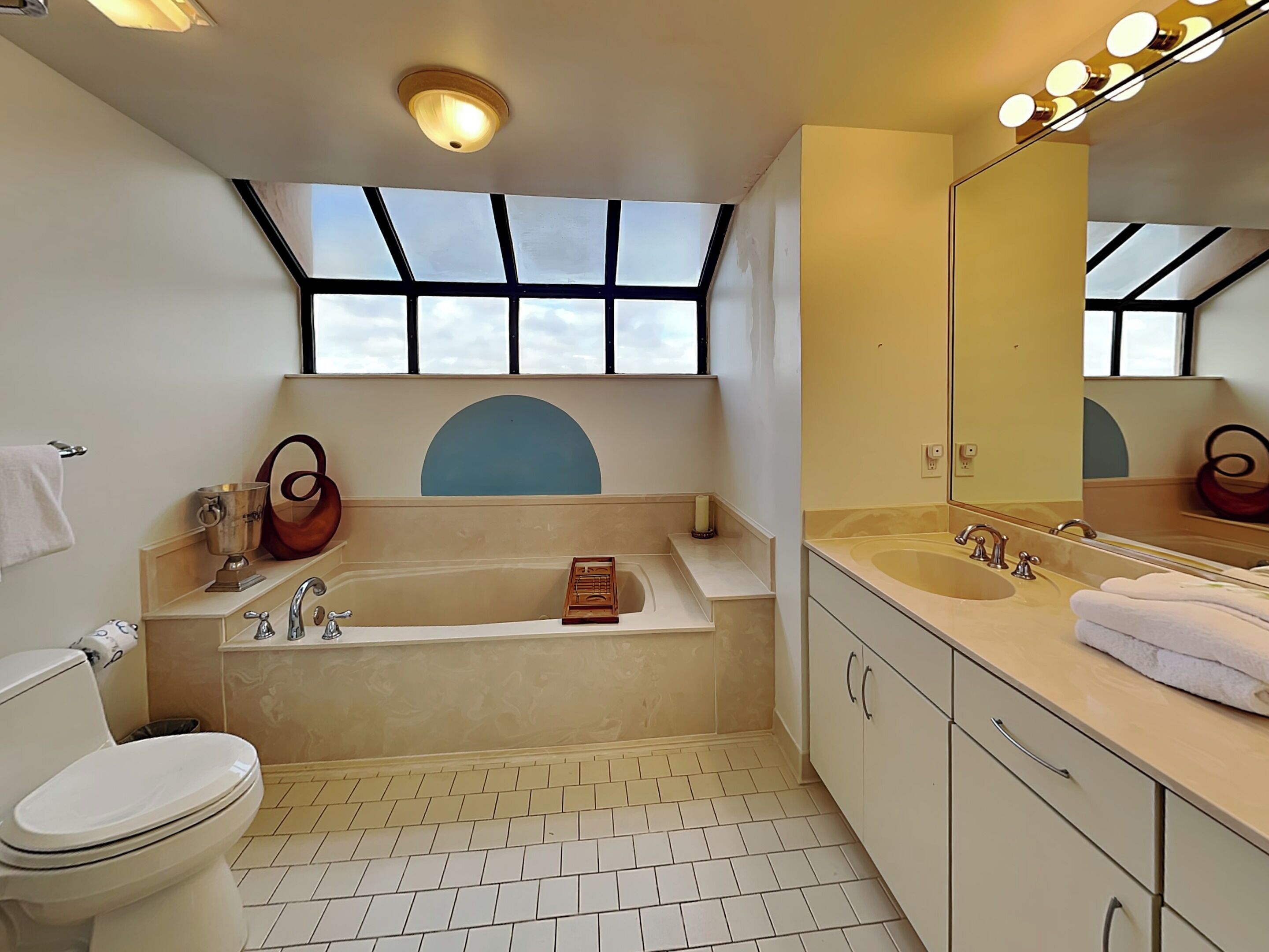 Une salle de bain moderne dotée d’une lucarne, d’une baignoire, d’un grand miroir et de toilettes.