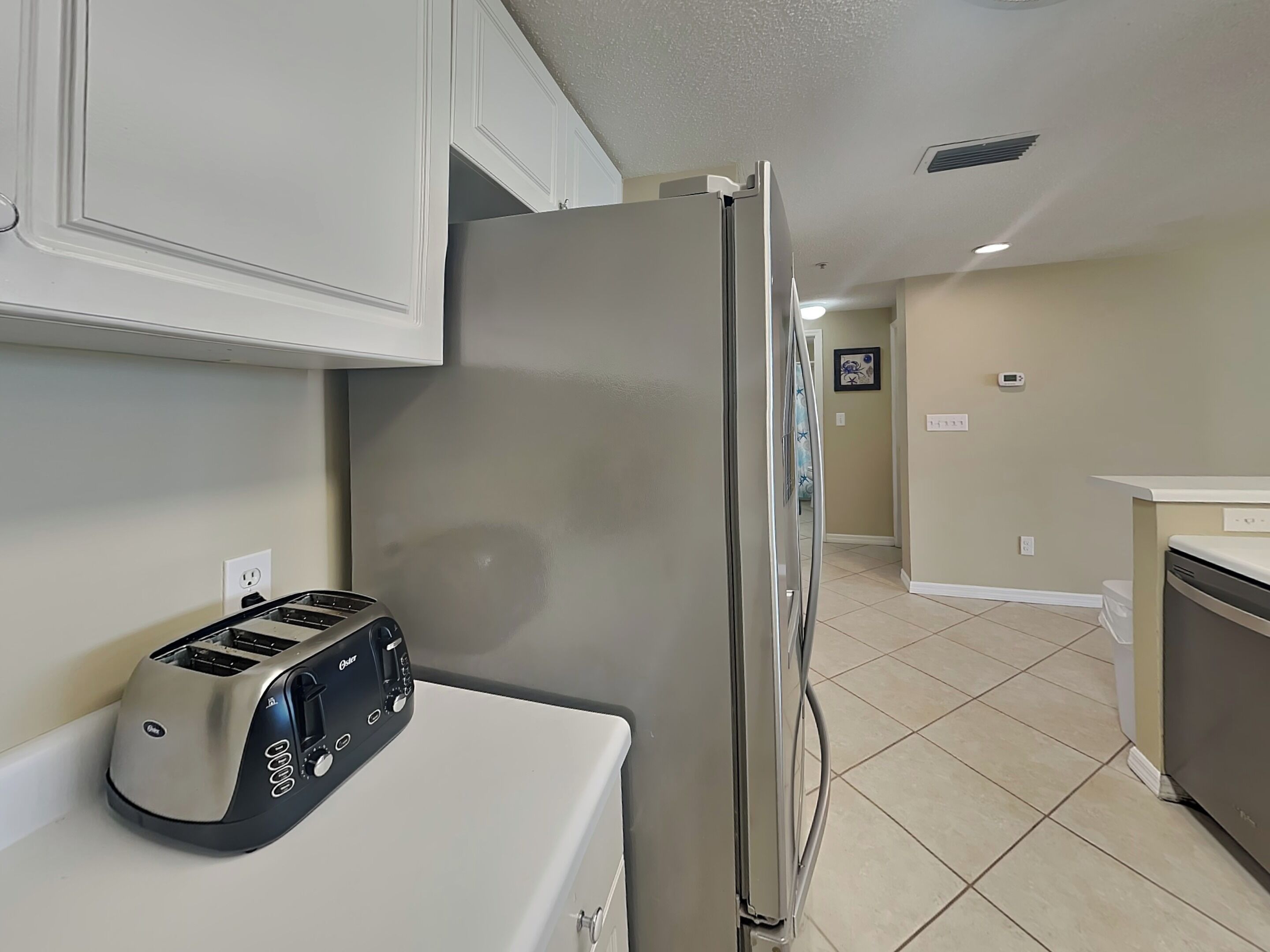 Una cocina con un refrigerador de acero inoxidable, un tostador y una encimera blanca.