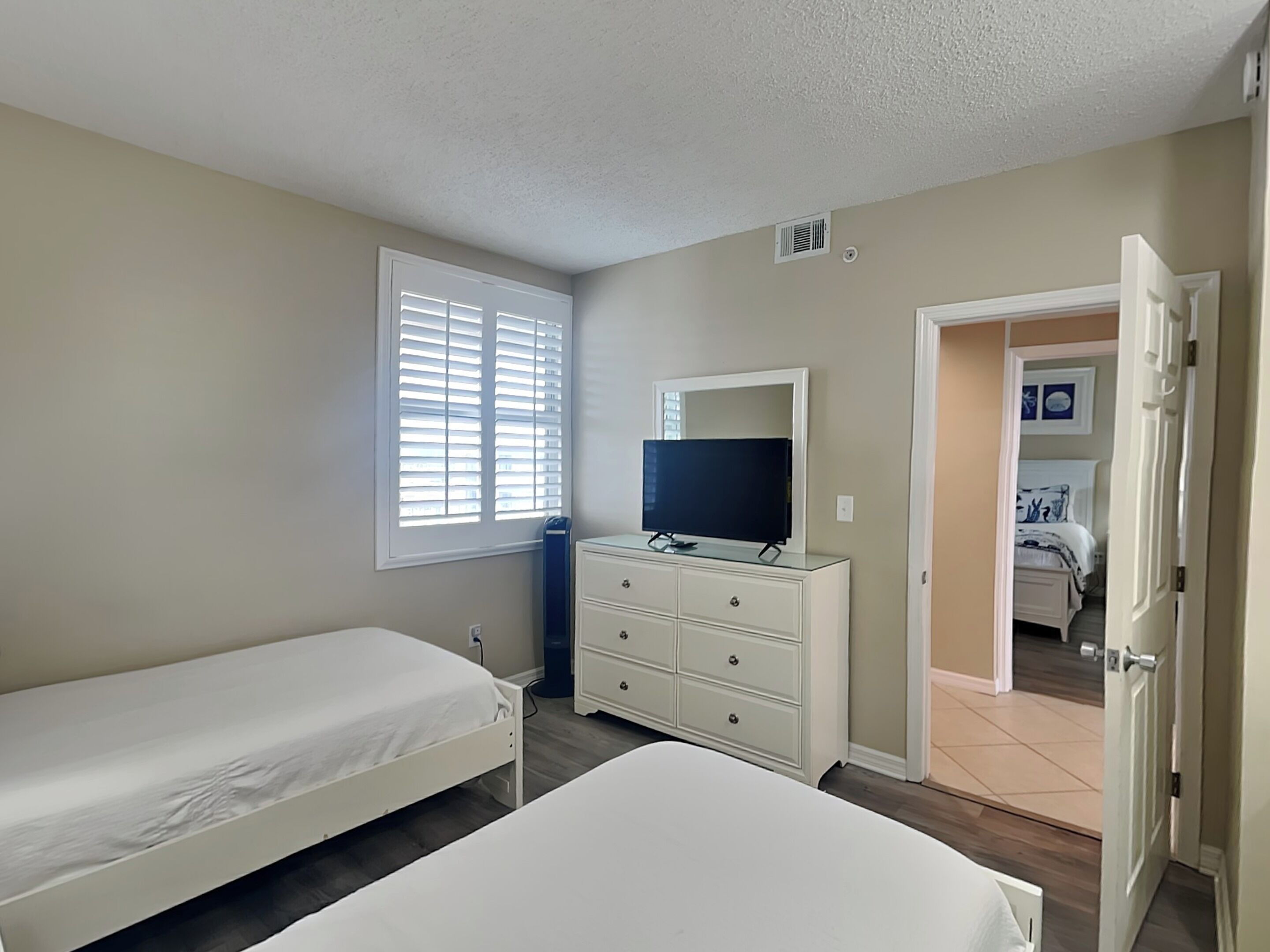 A bedroom with two single beds, a dresser, a television on top, and a window with blinds.