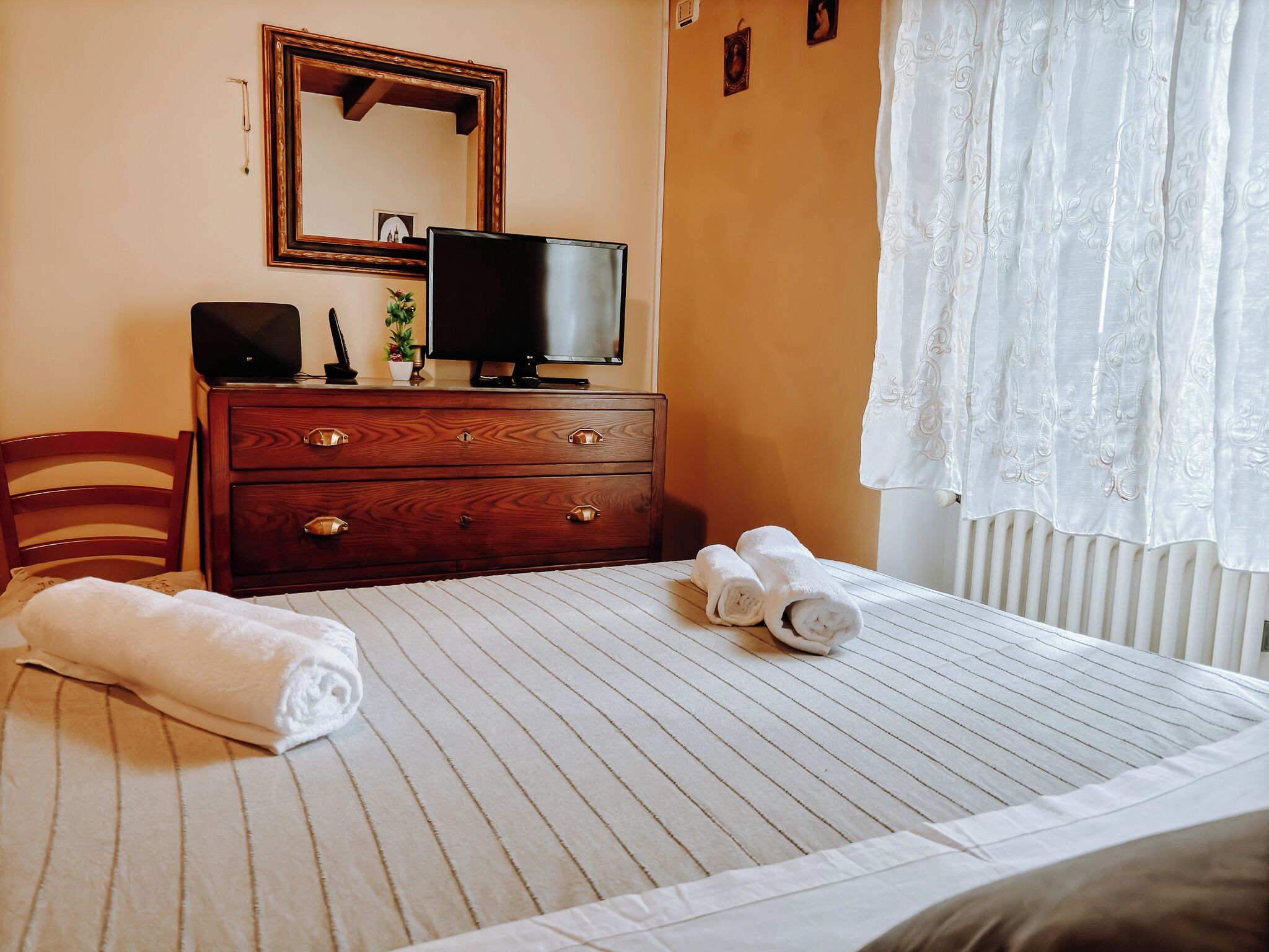 A neatly made bed with rolled towels, a wooden dresser with drawers, a television, and a mirror on the wall.