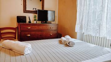 A neatly made bed with rolled towels, a wooden dresser with drawers, a television, and a mirror on the wall.