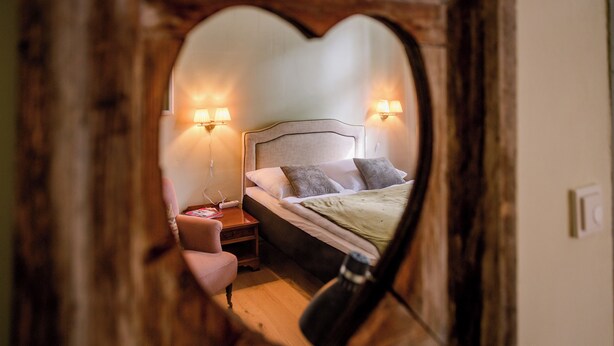 A bedroom with a heart-shaped mirror, a bed with pillows, a nightstand, and wall-mounted lamps. - Stylish accommodation in a monument in the heart of Halberstadt's old town (Halberstadt)