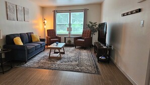 A living room with a dark blue sofa, two armchairs, a coffee table, and a television. - 12-On-North - Unit 528 #2 (niles)