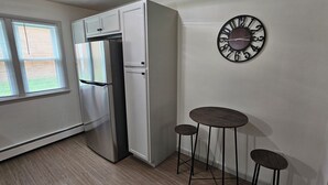 A compact kitchen with white cabinets, a stainless steel refrigerator, a wall clock, and two stools. - 12-On-North - Unit 528 #2 (niles)
