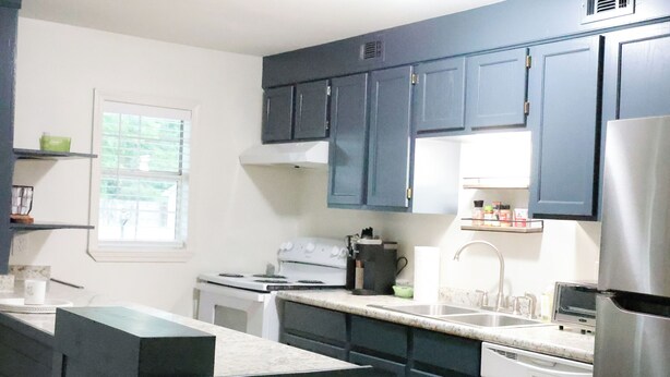 A kitchen with dark blue cabinets, a white stove, a sink, and a refrigerator.