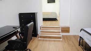A bedroom with a bed, a desk with a chair, and a staircase leading to another room.
