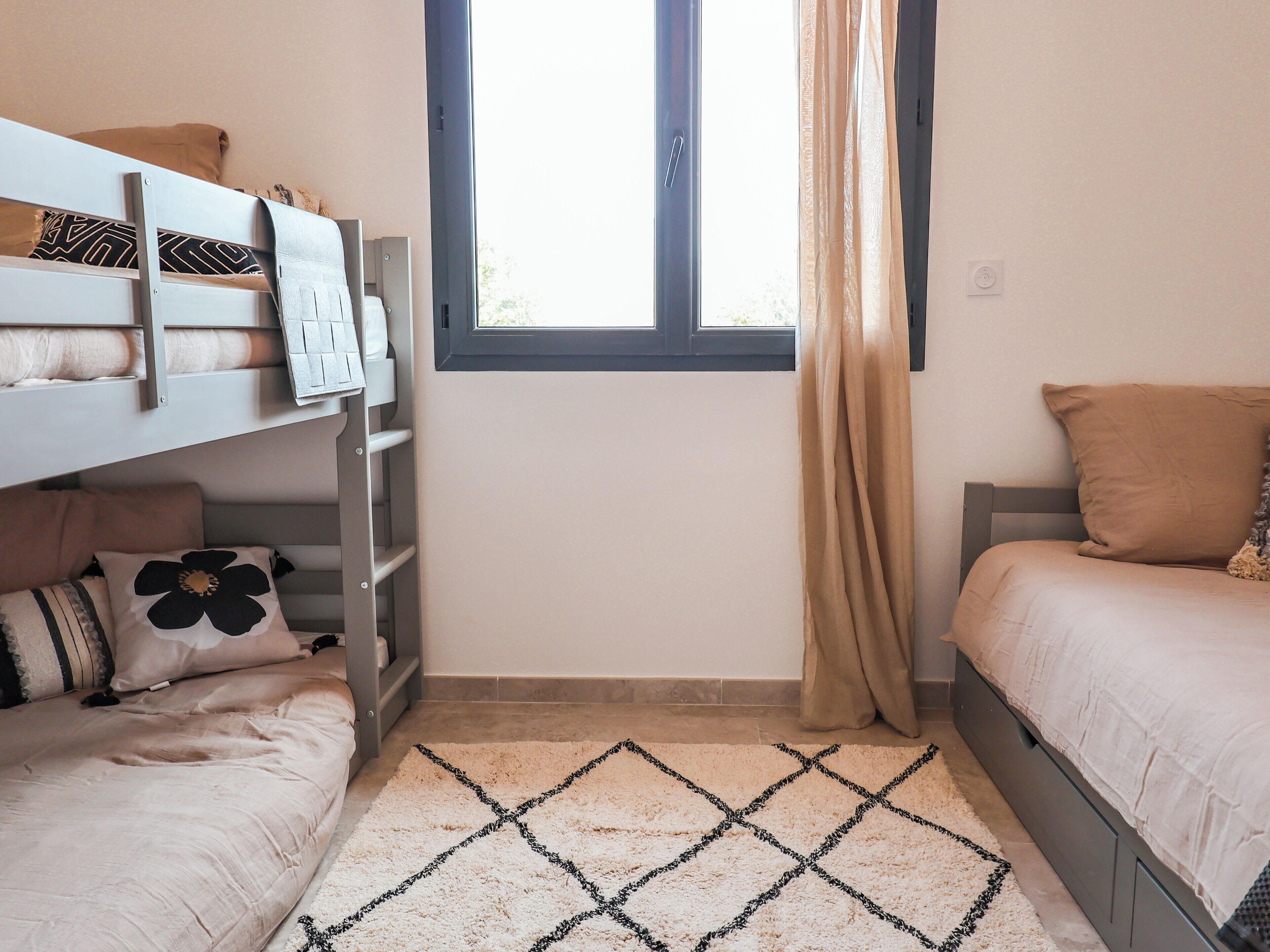 A bedroom with bunk beds, a window with curtains, and a patterned rug.