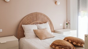 A bedroom with a wicker headboard, white bedding, and a bedside table with a vase of flowers.