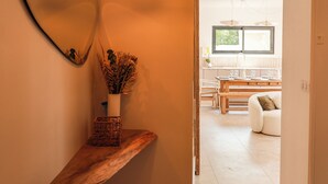 A hallway leading to a dining area with a wooden bench, a mirror, and a vase with dried flowers.