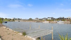 A waterfront property with a wooden dock extending into calm water, surrounded by residential buildings and a small boat docked nearby.
