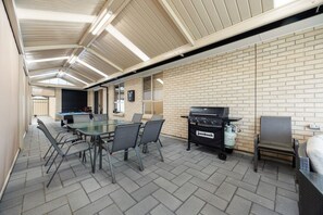 Een binnenterras met een bakstenen muur, een glazen tafel en stoelen.