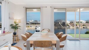 A modern dining area with a large table and chairs, a potted plant, and a view of a marina through large windows.