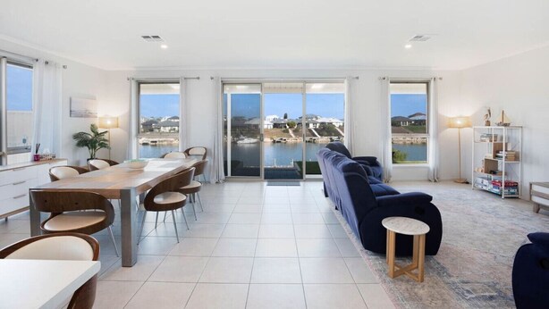A spacious living area with a dining table and chairs, a sofa, and a view of a marina through large sliding doors.