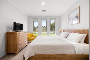 A bedroom with a bed, a TV on a wooden dresser, a yellow chair, and a window with a view.
