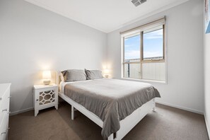 Een slaapkamer met een bed, nachtkastjes, een dressoir en een raam met uitzicht.