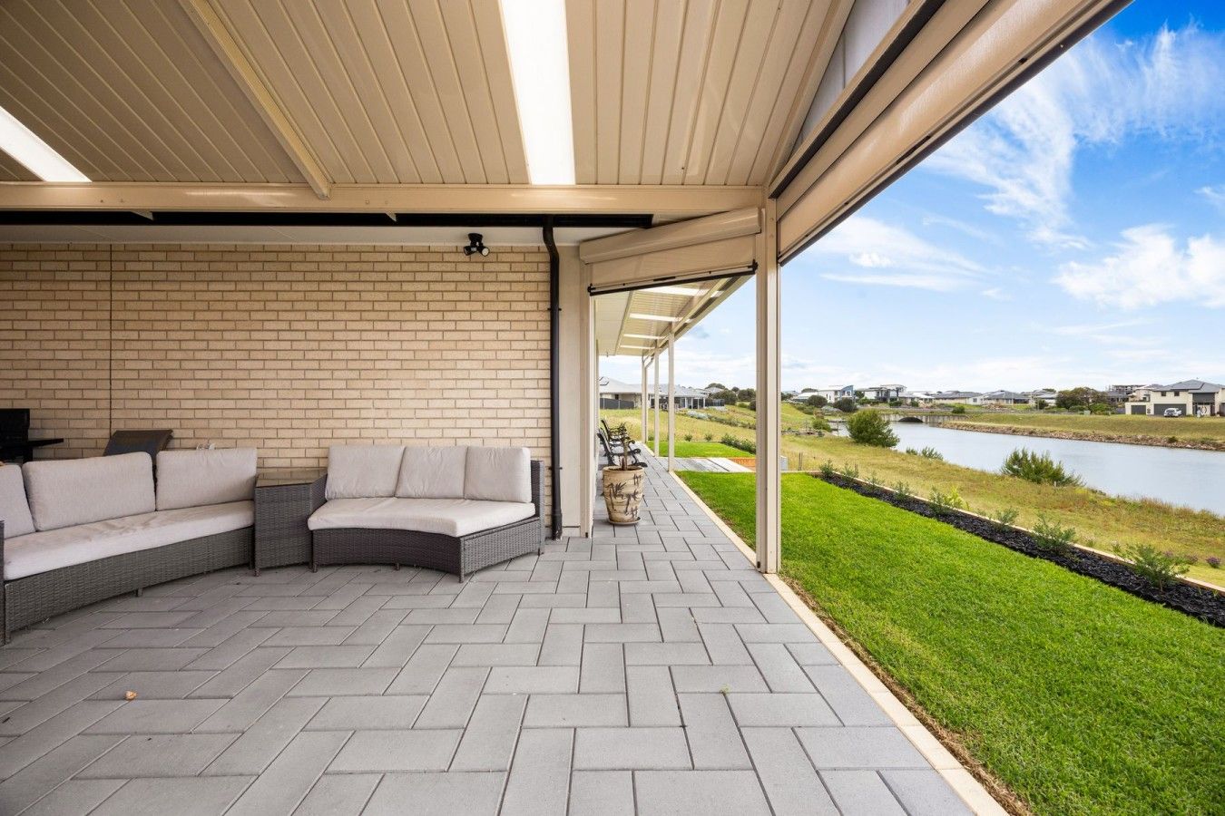 Un patio couvert avec un mur en briques, un canapé et une vue sur une étendue d’eau et des maisons au loin.