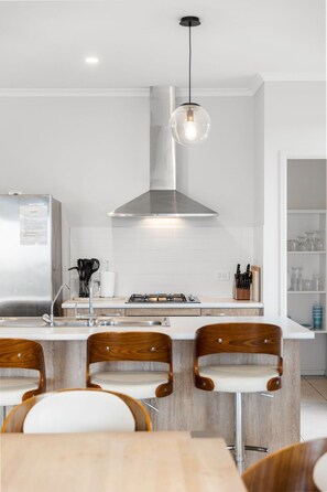 Een moderne keuken met een centraal eiland, roestvrijstalen apparatuur en houten stoelen.