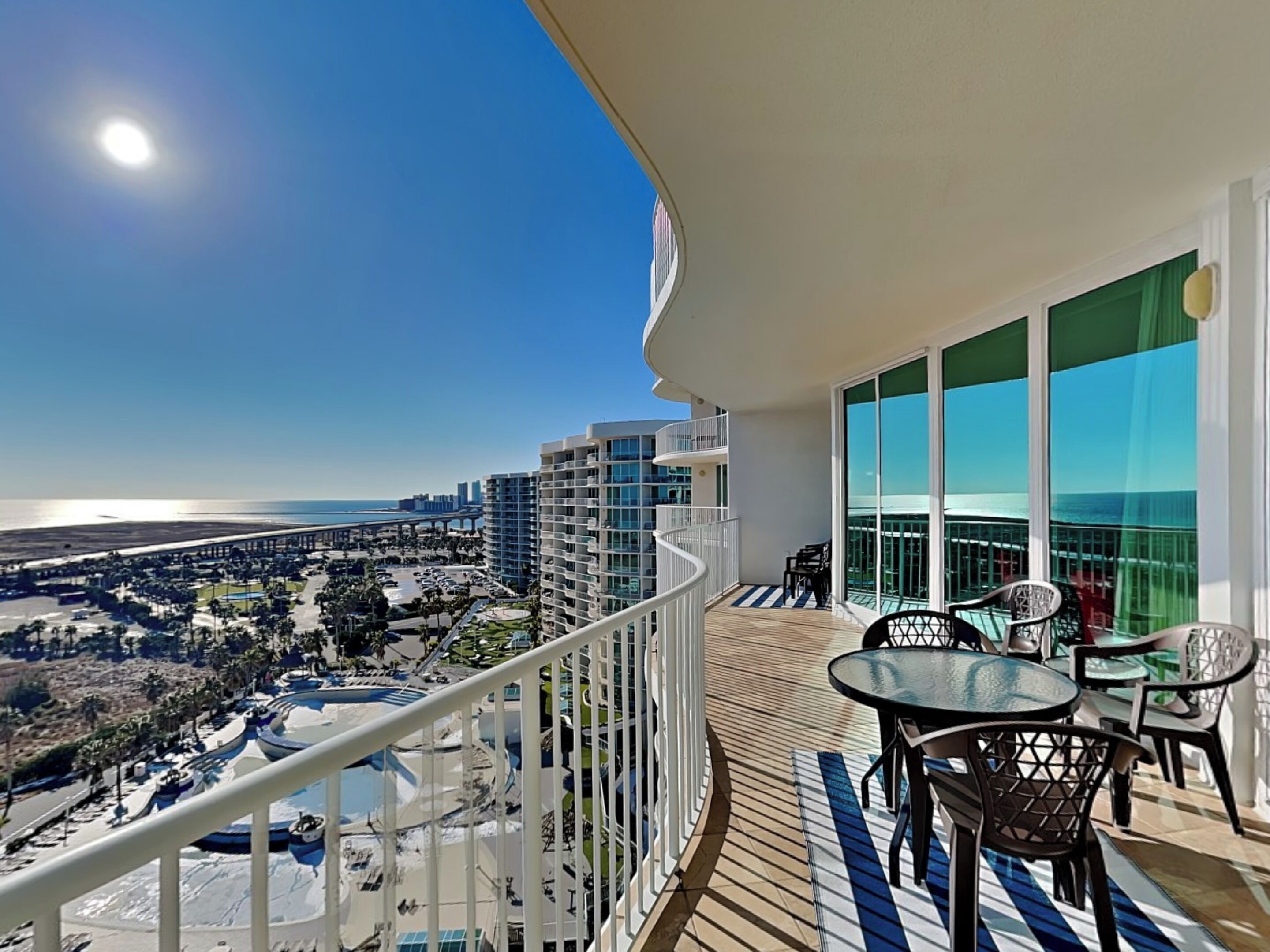 A balcony with a view of a beach and cityscape, featuring a table and chairs.