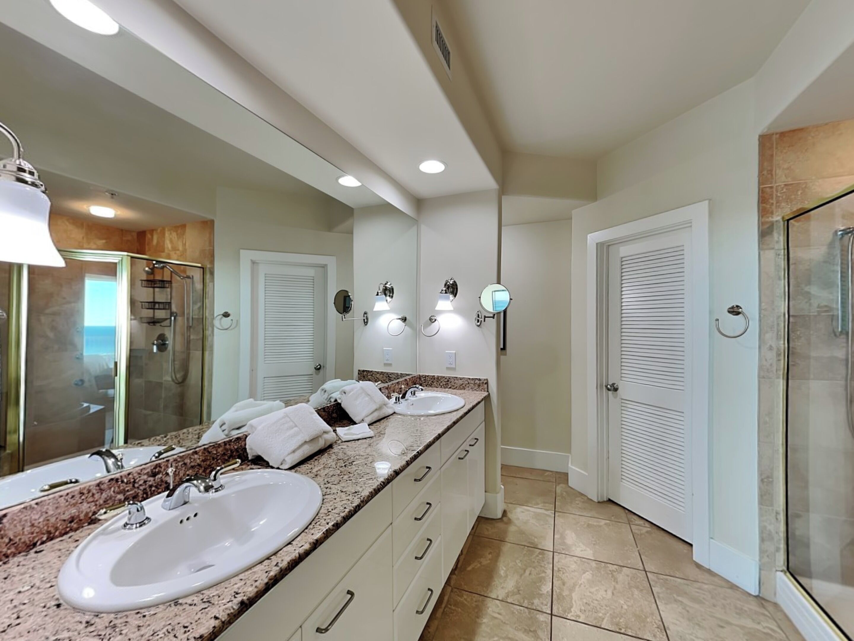 A modern bathroom with two sinks, a glass shower enclosure, and a large mirror.