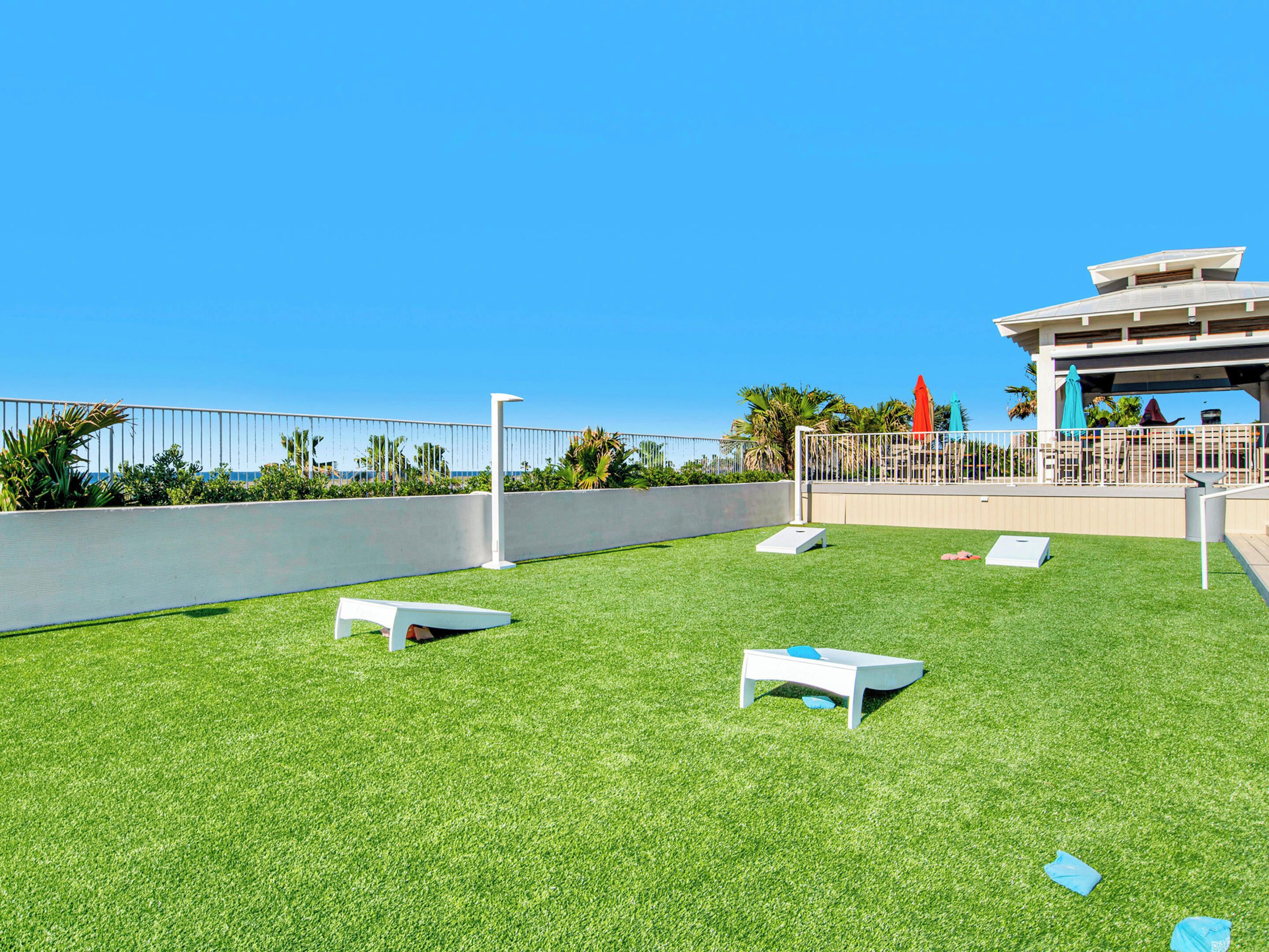 A rooftop terrace with artificial grass, a white bench, and a covered seating area with umbrellas.