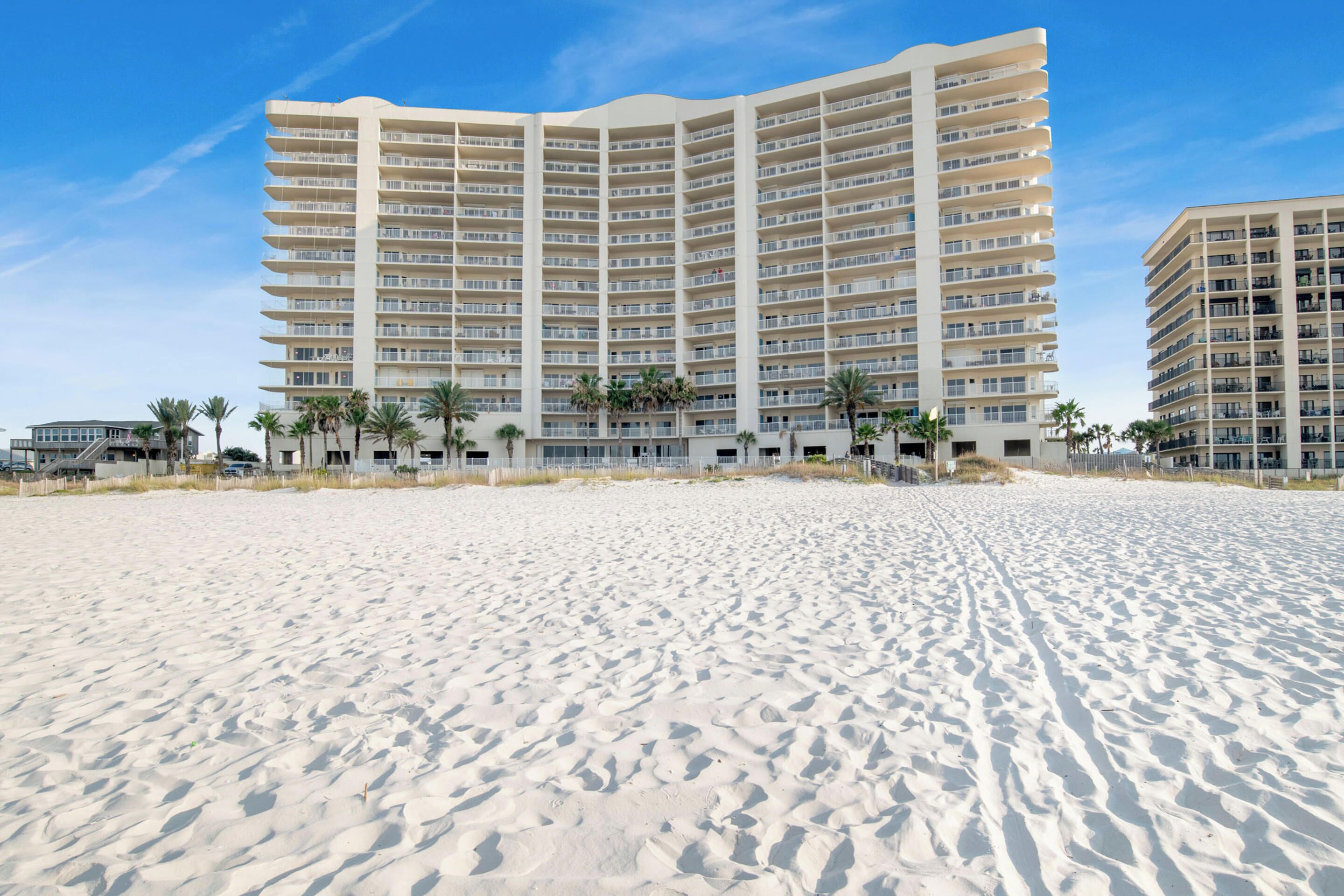 A beachfront hotel with multiple floors, palm trees, and a sandy beach.