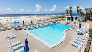 A pool area with lounge chairs and umbrellas, a beach in the background, and a clear sky. - Sea Oats #603 by Southern Vacation Rentals (Fort Walton Beach)